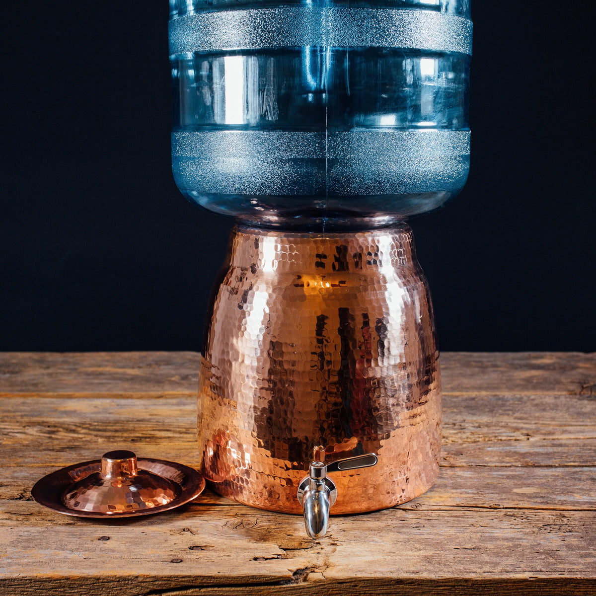 Sertodo Niagara copper water dispenser with water jug on a wooden table
