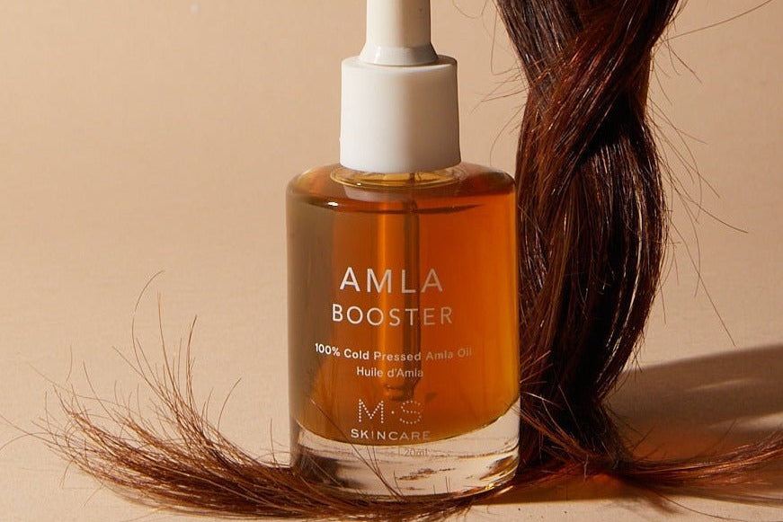 AMLA Booster skincare oil bottle with a dropper on a beige background with hair strands.