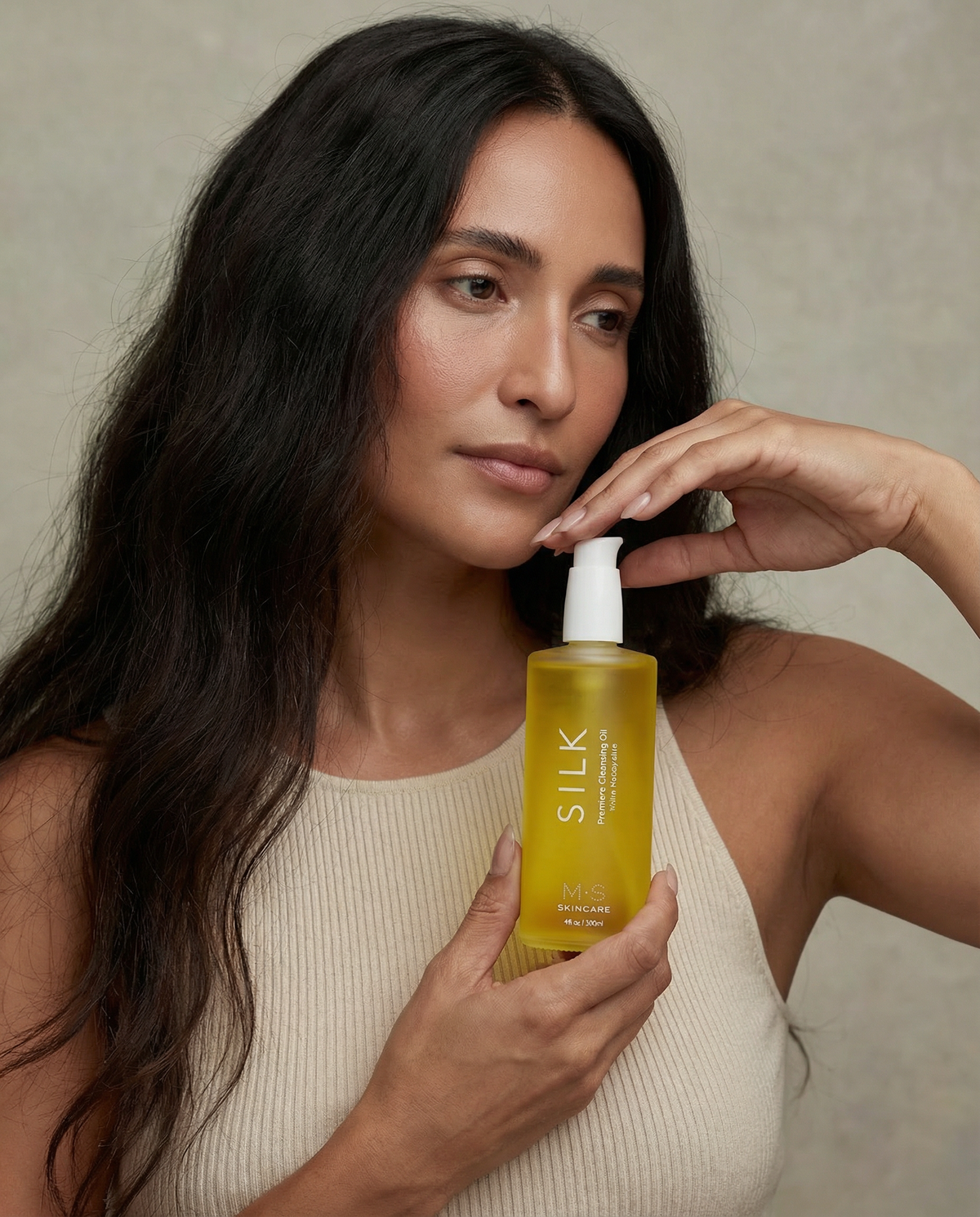 Woman in a cream sweater holding Silk Cleansing Oil