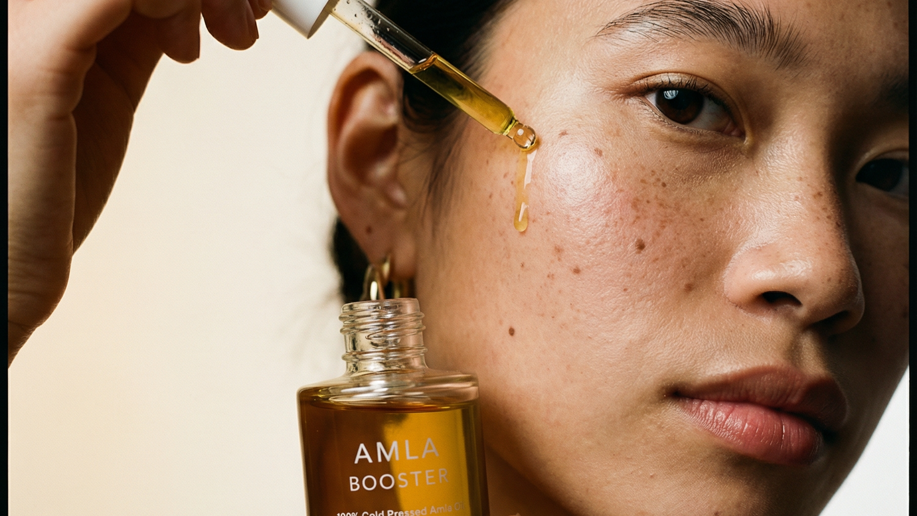 Person applying AMLA Booster serum to their face with a dropper.